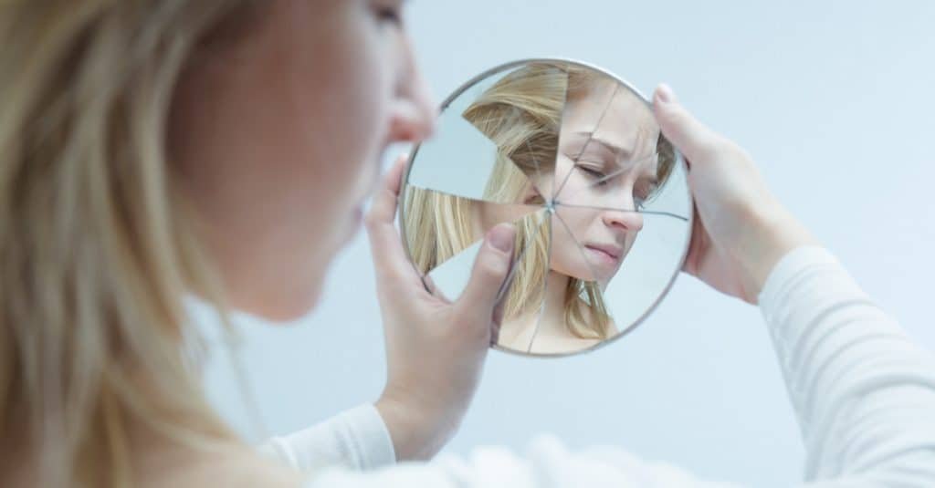 desolated young woman looking into a broken mirror which she is holding in her hands