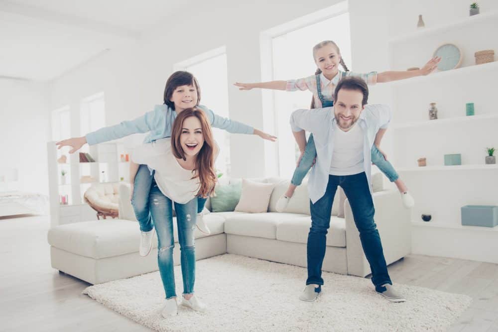 cheerful positive parents playing with kids in modern white apartments holding 