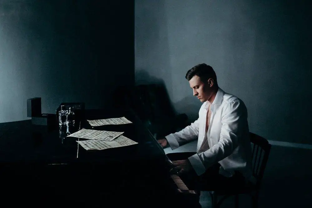handsome man in an unbuttoned white shirt is playing on a black piano