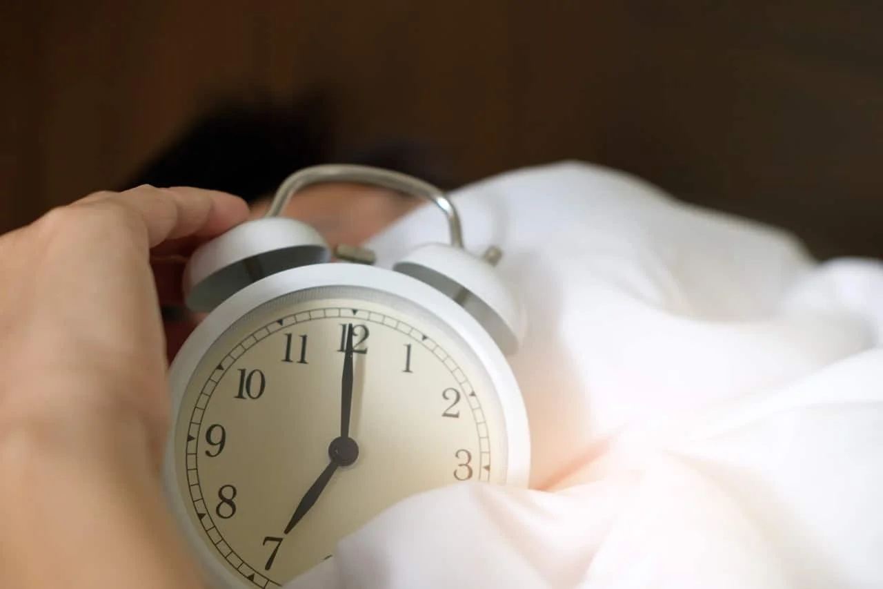 person holding alarm clock in his bed