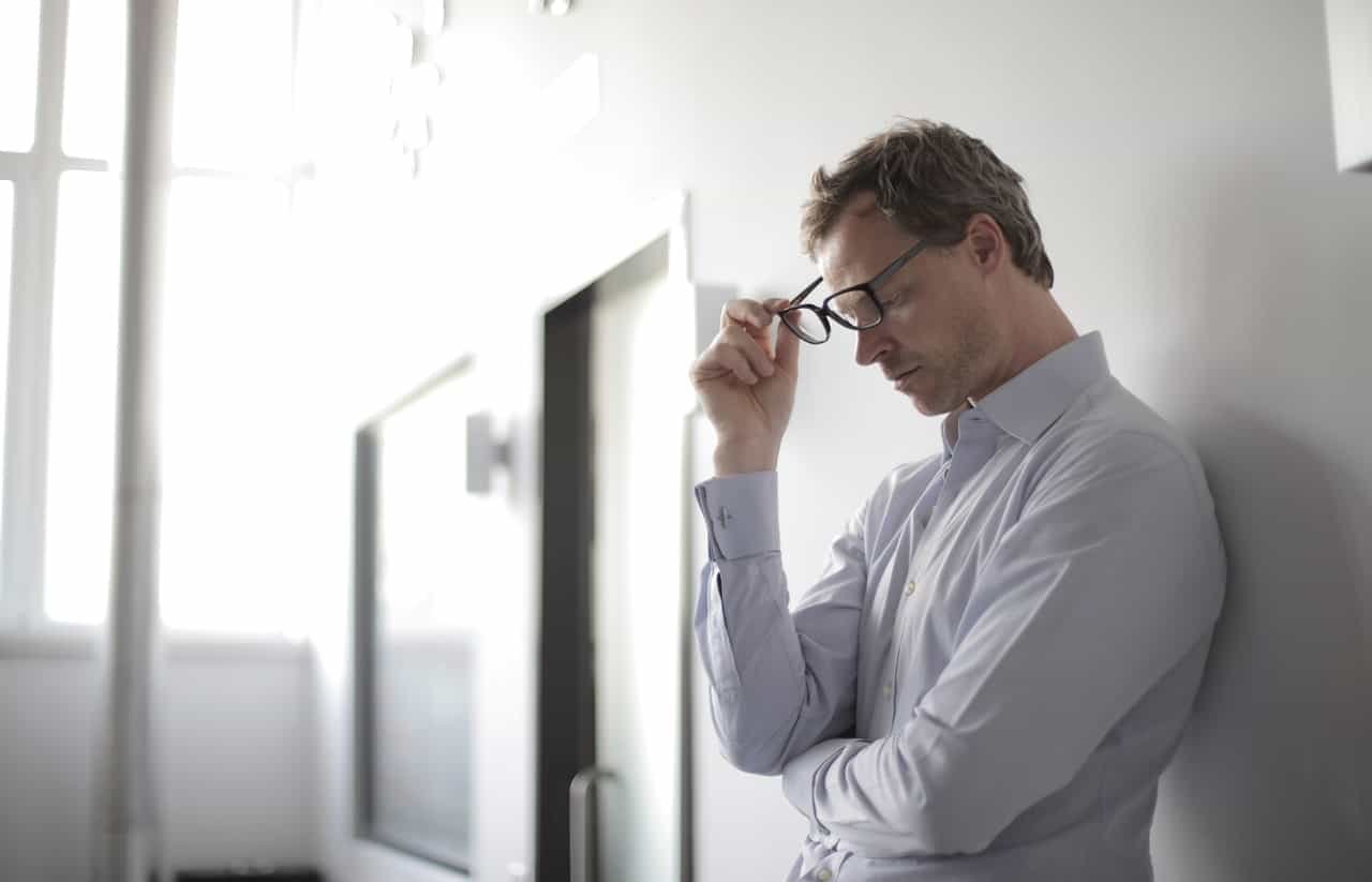 stressed man holding black eyeglasses and thinking