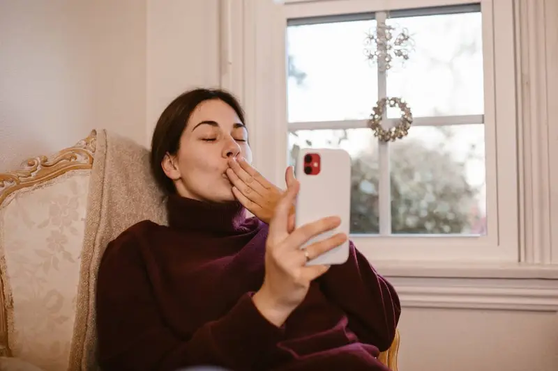 young women blowing kiss on phone while sitting on chair