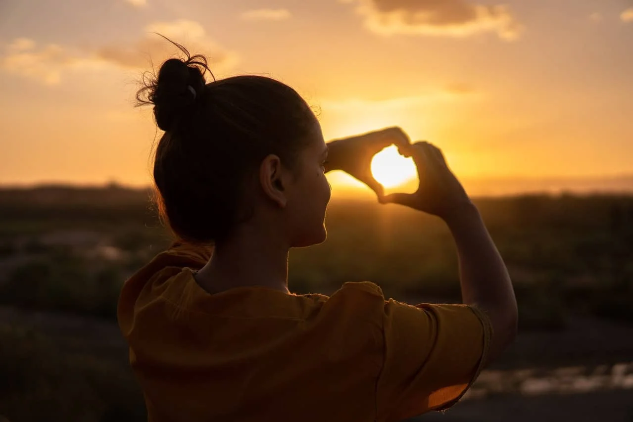 women doing hand heart sign during sunset