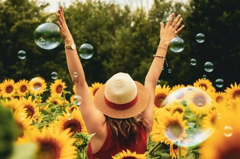 happy woman with raised arms amid sunflowers