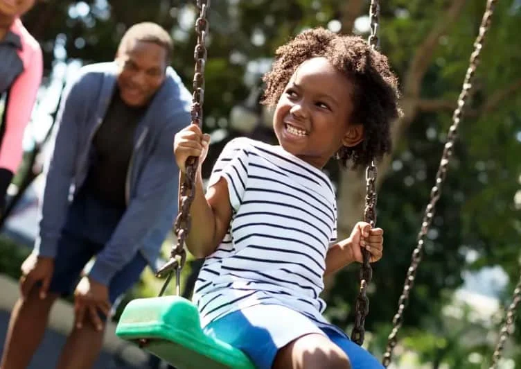 kid having fun on swing with parents in the background