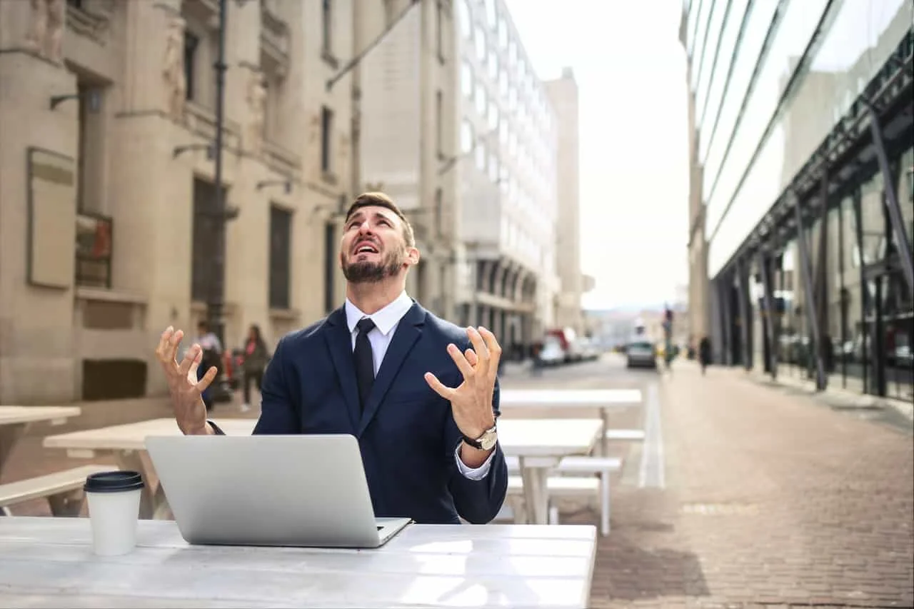 man in suit showing distress outdoor while using laptop