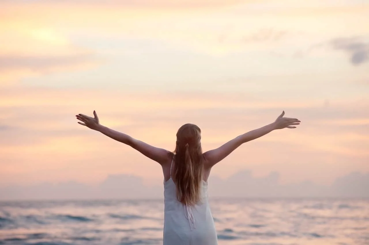 rear view of woman with arms raised at beach