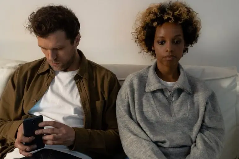 sad woman sitting beside man looking at smartphone