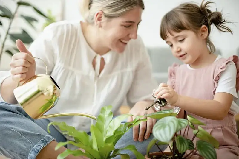 mother and daughter watering potted plant in home