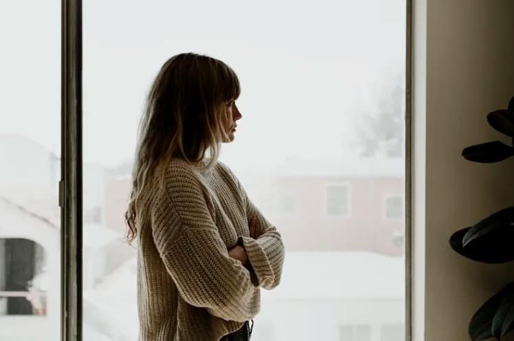 woman with arms folded staring out a window