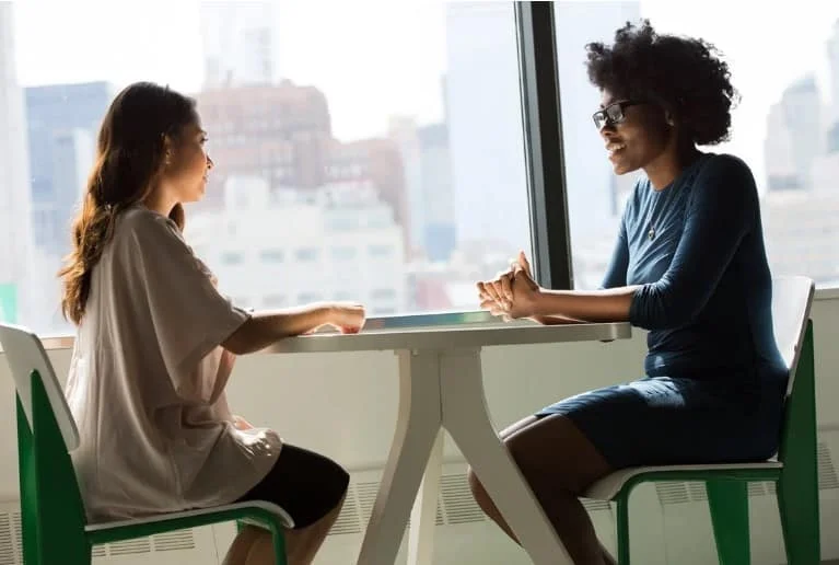 women sitting and conversing beside a window