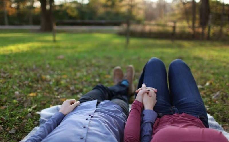 couple holding hands while lying in a field