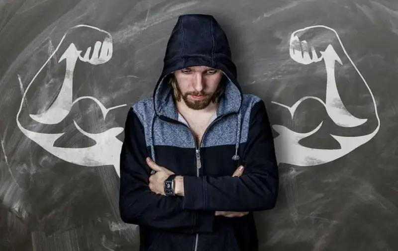 man standing in front of a board with a drawing of big biceps