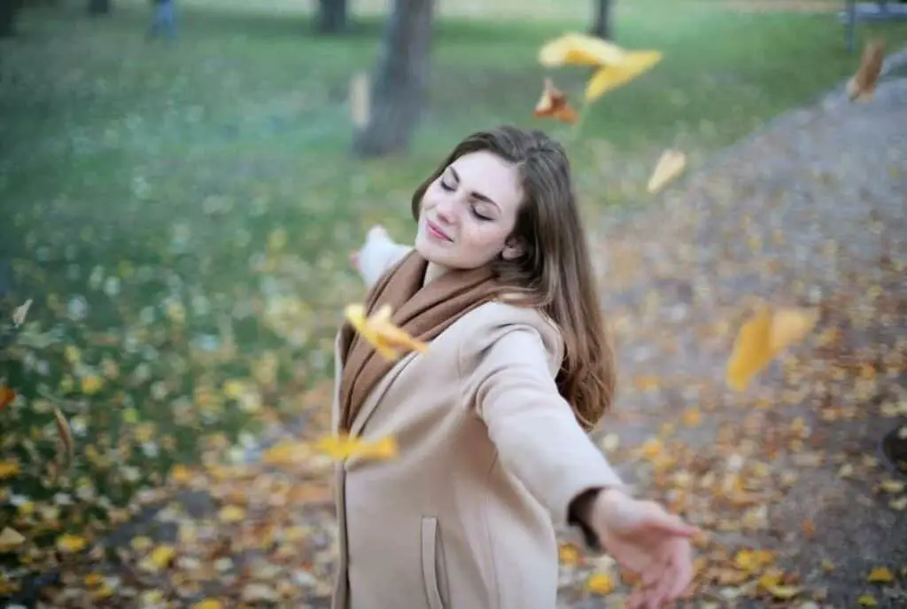 smiling woman with eyes closed spreading her arms in a park