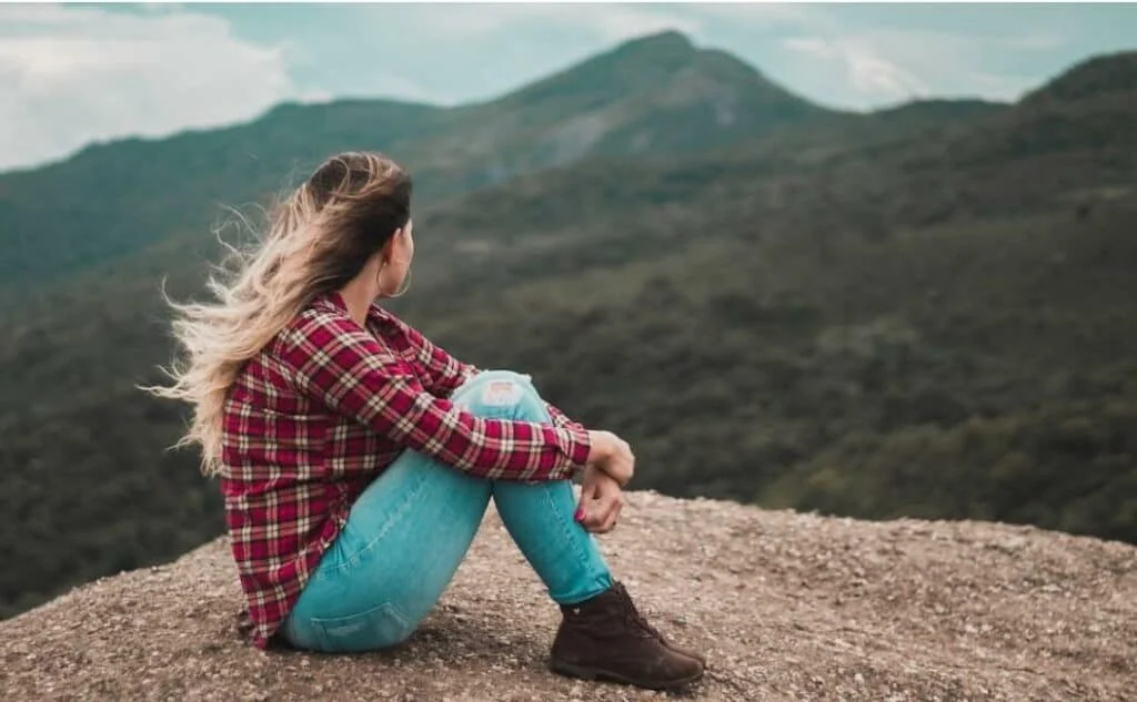 woman sitting on the ground overlooking a hill