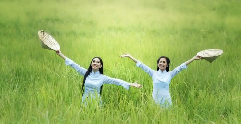 women hold hats and spread their arms in a green field