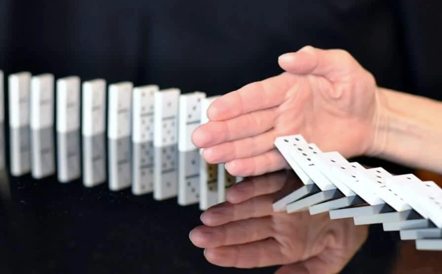 hand interrupting falling dominoes