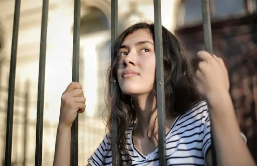 woman looking hopefully through an iron fence