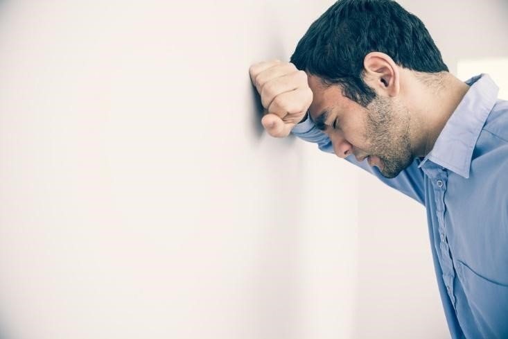 Anxious man with head against a wall