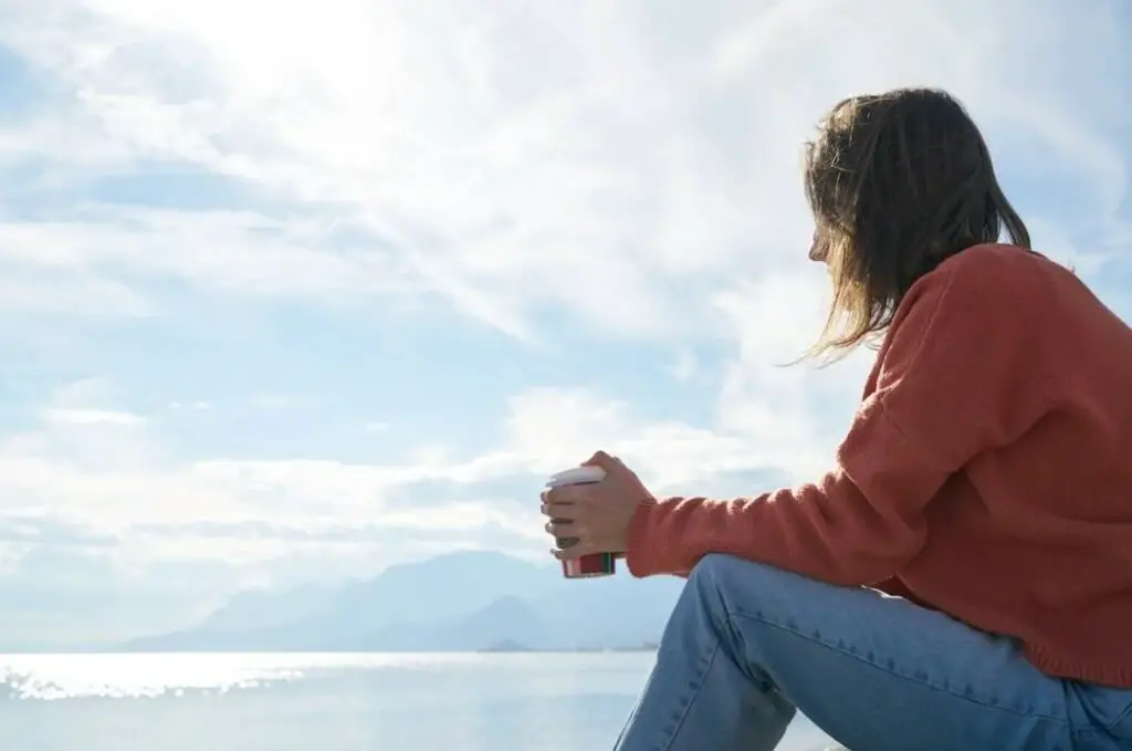 Woman holding a cup sitting by the seaside