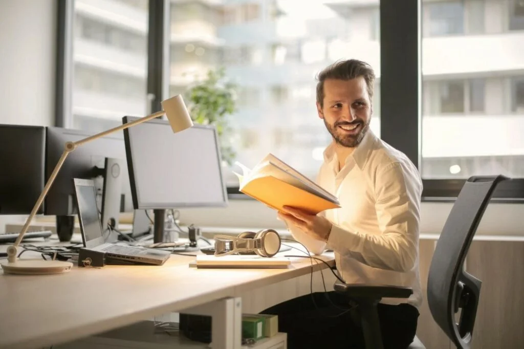 Smiling man holding a book at his desk